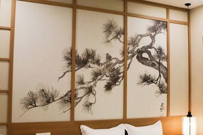 Una habitación tradicional japonesa con suelo de tatami, un bajo cabecero de madera y un shoji con una pintura de un pino.