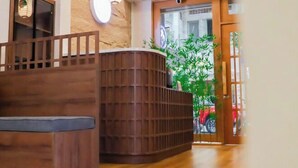 A reception area with a wooden reception desk, a wall-mounted light fixture, and a door leading outside. - KATOYA SUITES SAIGON HONKAN (Ho Chi Minh City)