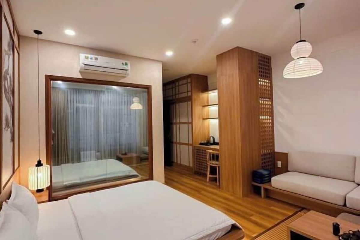 Ein Hotelzimmer mit Bett, Schreibtisch, Stuhl, Sofa und einem großen Fenster mit Vorhängen.