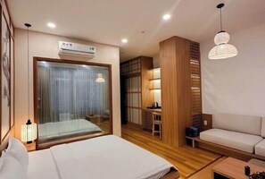 A hotel room with a bed, a desk, a chair, a sofa, and a large window with curtains. - KATOYA SUITES SAIGON HONKAN (Ho Chi Minh City)