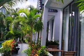 A building with a covered outdoor seating area, palm trees, and a clear sky.