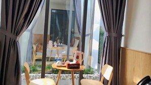 Une pièce dotée d’une grande fenêtre, d’une petite table ronde avec une machine à café, de deux chaises et donnant sur un espace extérieur aménagé avec une table et des chaises.
