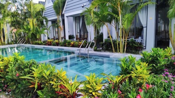 Une piscine entourée d’une végétation luxuriante et de bâtiments modernes dotés de grandes fenêtres.