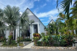 A modern house with a sloped roof, surrounded by tropical vegetation and a stone pathway.