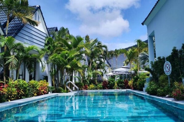 A swimming pool surrounded by palm trees and a building with a tiled roof.
