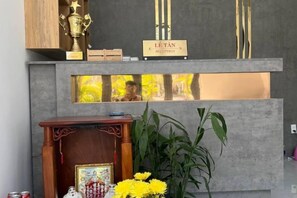 A reception desk with a wooden cabinet, a framed picture, and a potted plant.