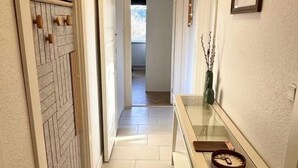 A hallway with a patterned door, a glass console table with decorative items, and a view into another room. - Ama Hyg Atelier (Copenhagen)