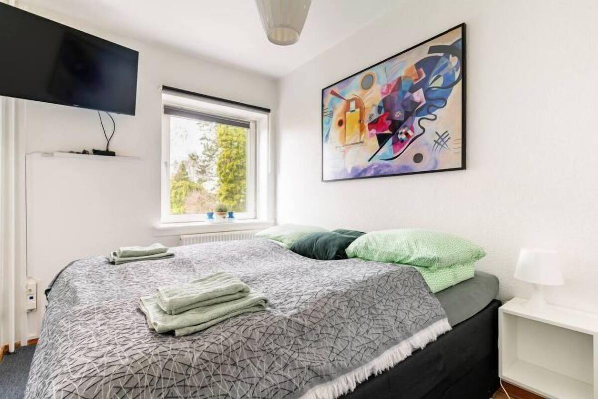 A modern bedroom with a bed, a TV, a window, and a painting.