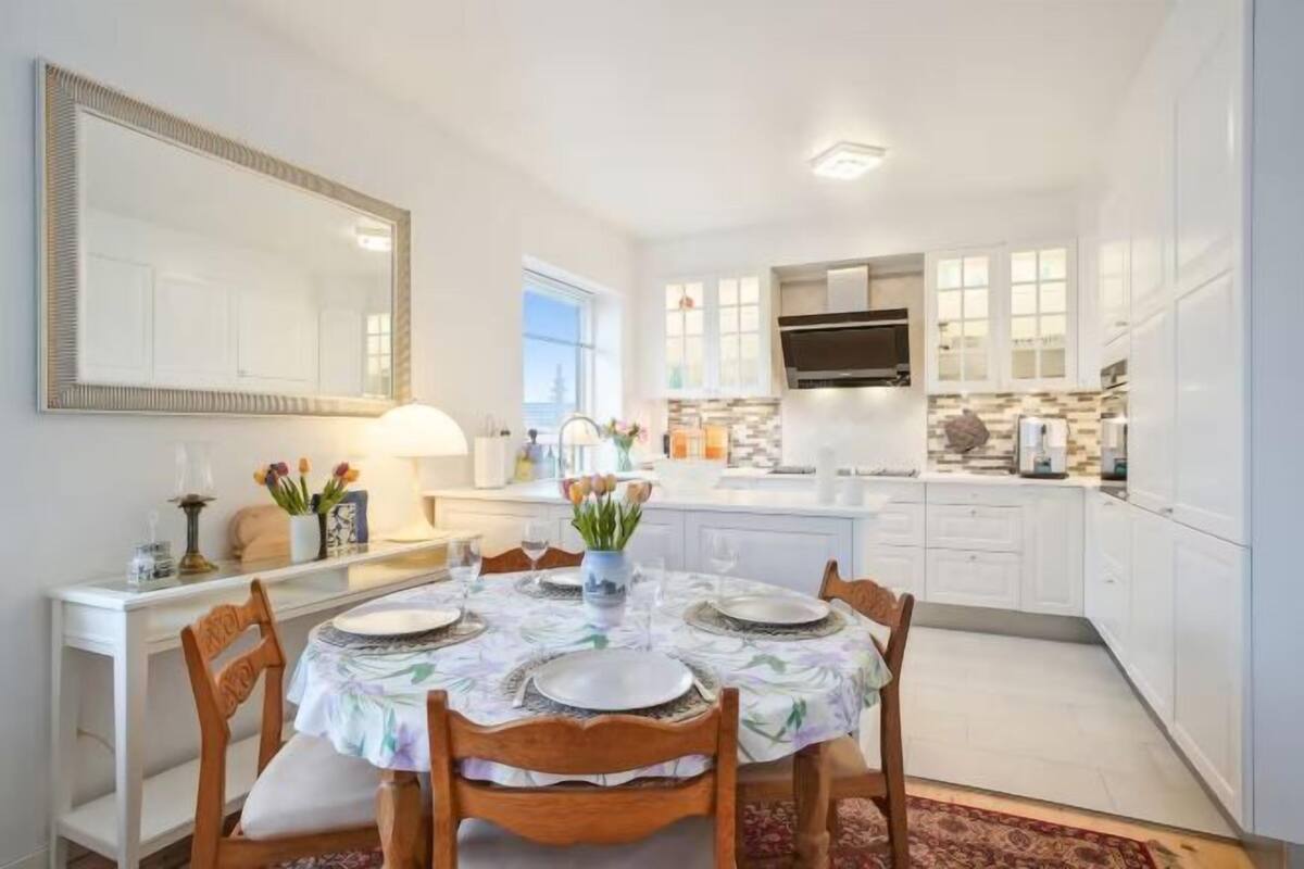 A modern kitchen with white cabinets, a large mirror, and a dining table set for four.