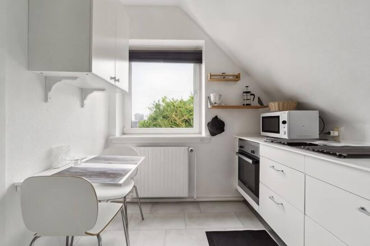 A compact kitchen with a dining table, white cabinetry, a microwave, and a window with a view of greenery.
