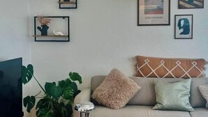 A living room with a sofa, decorative pillows, a plant, a TV, and wall art. - Ama Hyg Atelier (Copenhagen)