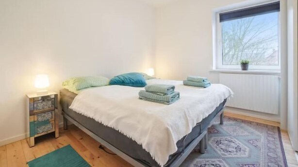 A bedroom with a bed, bedside tables, a window with a view, and a patterned rug. - Ama Hyg Atelier (Copenhagen)