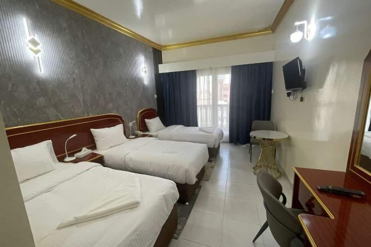 Een hotelkamer met twee bedden, een bureau, een stoel, een klein tafeltje, een televisie en een raam met gordijnen.