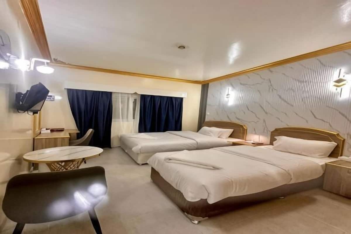 Een hotelkamer met twee bedden, een bureau, een stoel en een bijzettafeltje.