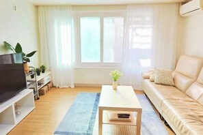 A living room with a TV, sofa, coffee table, and a window with curtains.