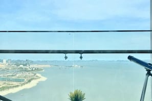 Blick aus einem Fenster mit einem Teleskop auf eine Küstenlandschaft mit Gebäuden und Strand.