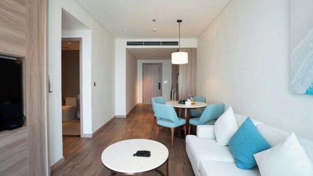 A modern living room with a white sofa, a round coffee table, and a dining area with chairs. - Alacarte Ha Long - Service Apartment (Ha Long)