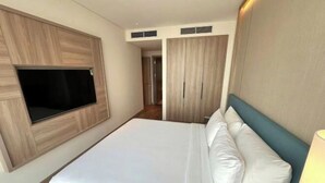 A hotel room with a large bed, a mounted TV, and a wardrobe. - Alacarte Ha Long - Service Apartment (Ha Long)
