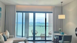 A modern hotel room with a balcony, a sofa, a dining table, and chairs. - Alacarte Ha Long - Service Apartment (Ha Long)