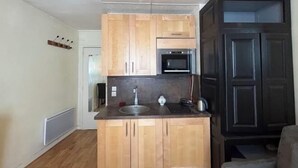 A compact kitchen with wooden cabinets, a stainless steel sink, and a microwave. - Vintage studio 150m to Notre Dame (Paris)