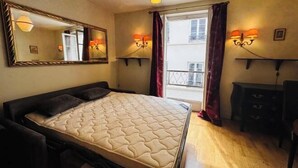 A bedroom with a bed, a dresser, a mirror, and two wall-mounted lamps. - Vintage studio 150m to Notre Dame (Paris)
