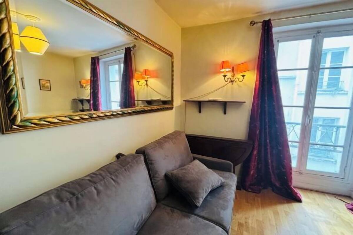 A living room with a sofa, a large mirror, wall-mounted lamps, and a window with curtains.