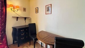 A small dining area with a wooden table and two chairs, a dark wooden cabinet, and wall-mounted lamps. - Vintage studio 150m to Notre Dame (Paris)