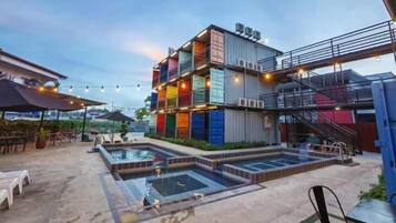 A rooftop pool area with a multi-tiered structure made of colorful shipping containers, surrounded by lounge chairs and umbrellas.
