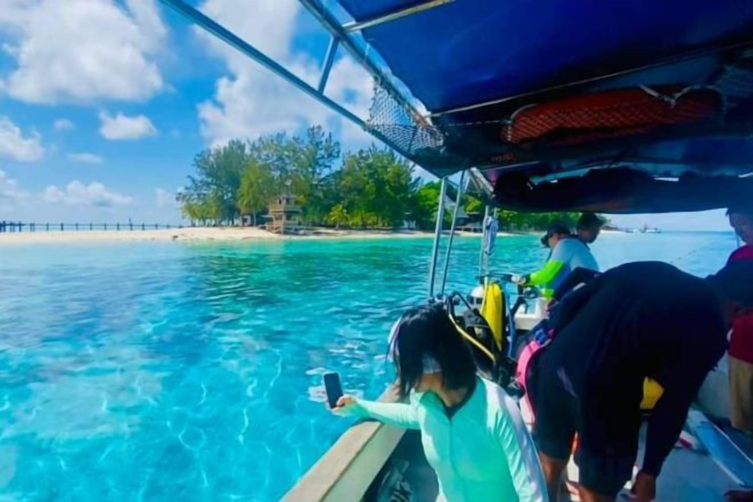 A boat with passengers, clear blue water, and a beach in the background.
