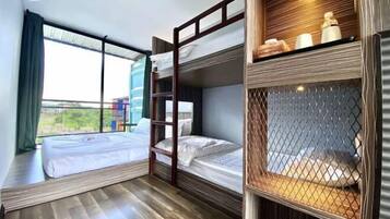 A modern hotel room with a large window, a bunk bed, and a wooden shelf with toiletries.