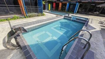 A swimming pool with a metal ladder, surrounded by a tiled deck.