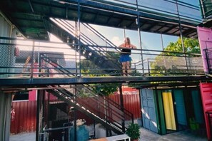 Área externa com vários níveis, escada de metal e uma pessoa no andar superior.
