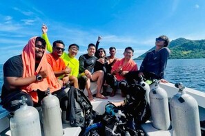 A group of people on a boat with scuba diving equipment and a clear view of the water and hills in the background. - BOX INN SEMPORNA (Semporna)