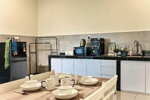 A modern kitchen with a dining table set with plates and cups, a coffee machine, and a refrigerator.