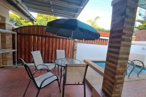 En uteplats med ett bord och stolar, en pool och ett takförsett område.