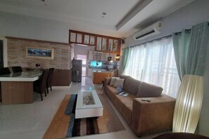 A modern living room with a sofa, coffee table, and a dining area with chairs. - Jacuzzi Pool Villa (Pattaya)