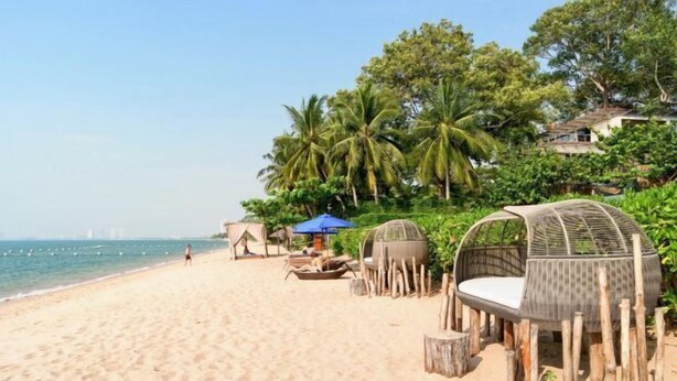 A beach with a wooden structure, a blue umbrella, and a person walking. - Jacuzzi Pool Villa (Pattaya)
