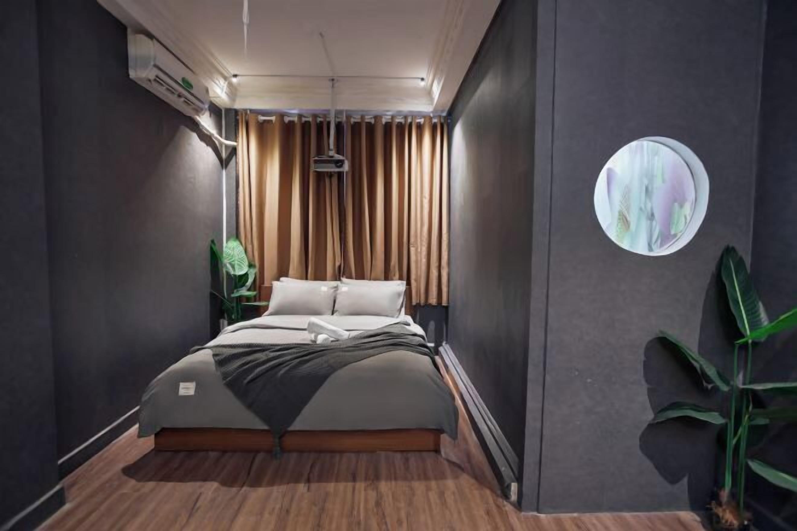 A modern bedroom with a bed, dark walls, a circular wall decoration, and a plant.