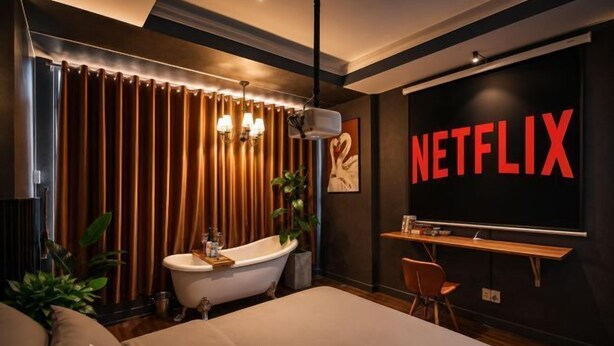 Una camera da letto moderna con un letto grande, una toeletta con vasca, una scrivania e una TV a parete che mostra il logo Netflix.