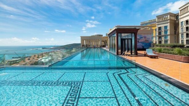 Piscina infinita en la azotea con vistas despejadas al mar, un área de estar cubierta y un edificio moderno con balcones.