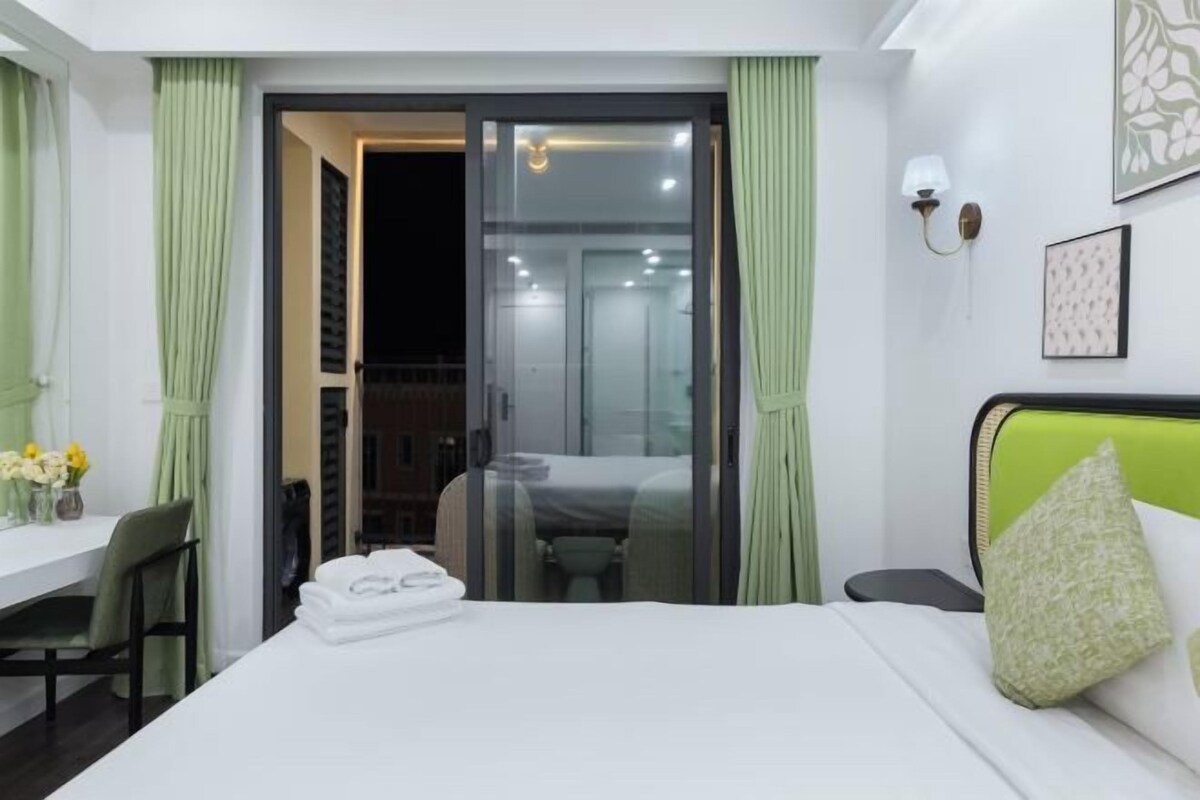 Een hotelkamer met een bed, een bureau met stoel, een kleine tafel met bloemen en een schuifdeur naar een balkon.