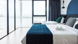 A hotel room with a large window, a bed with a blue blanket, and a view of the city.