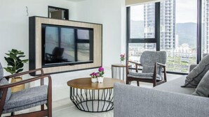 A modern living room with a large TV, comfortable seating, a round coffee table, and a view of a cityscape through large windows.