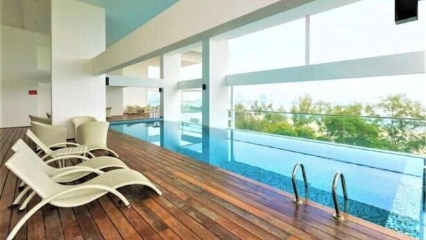 A modern indoor pool area with wooden flooring, lounge chairs, and a glass barrier overlooking a natural landscape.