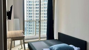 A bedroom with a bed, a small table, and a view of high-rise buildings through a large window. - Super Cozy and Clean Apartment connected to mall (West Jakarta)