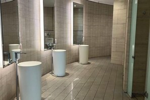 Ein modernes Badezimmer mit drei Waschbecken, großen Spiegeln und gefliestem Boden.