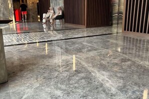 Un sol en marbre poli orné d’un motif géométrique au centre, un espace détente avec des chaises, et une personne qui marche au loin.