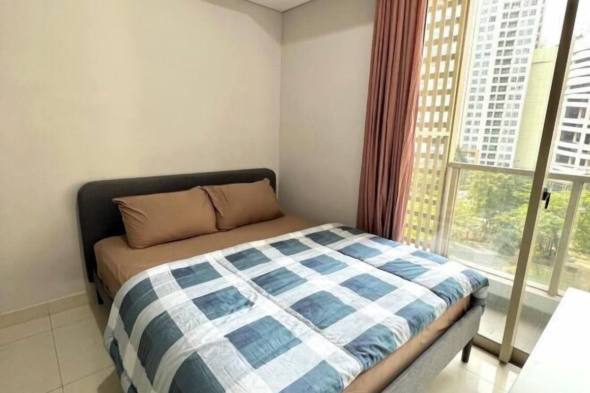 A bedroom with a bed, a window with a view of buildings, and a curtain.