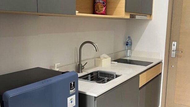 A compact kitchen with a sink, a blue refrigerator, and a wooden shelf above the sink. - Super Cozy and Clean Apartment connected to mall (West Jakarta)