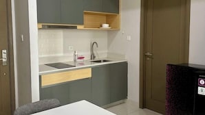 A compact kitchen with grey cabinets, a white countertop, a sink, and a small wooden shelf. - Super Cozy and Clean Apartment connected to mall (West Jakarta)